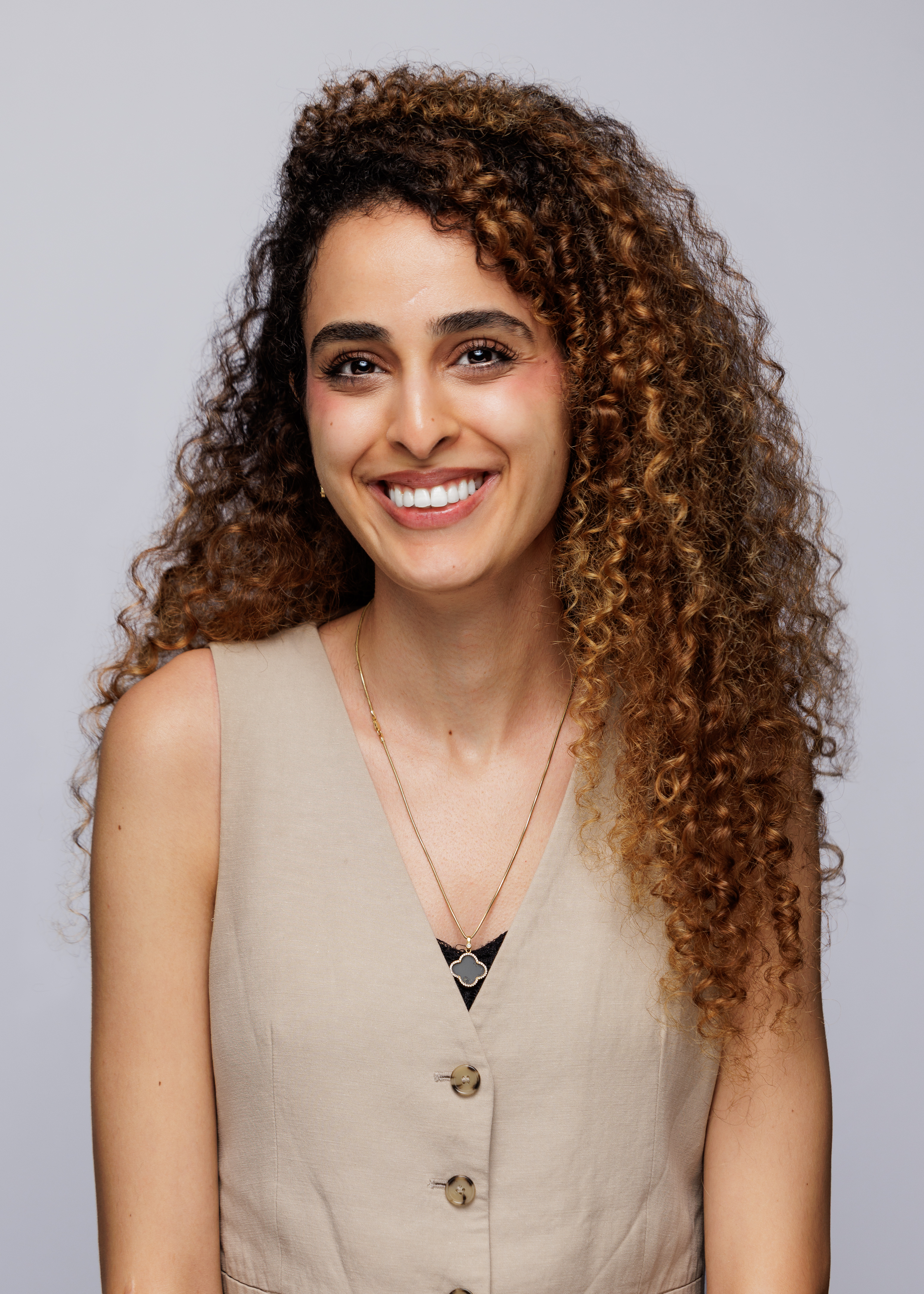 this is me smiling, wearing a beige vest and behind me is a grey background